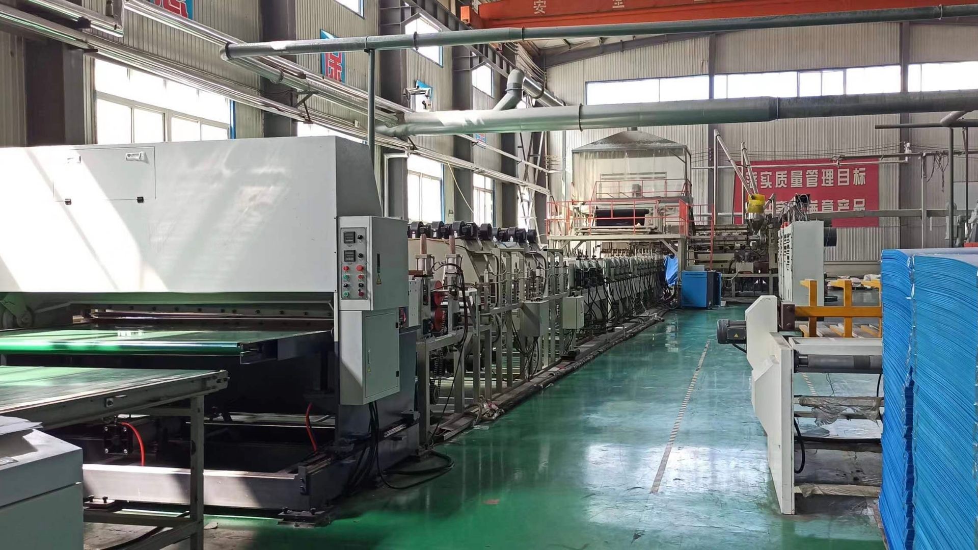 Interior of an industrial manufacturing facility with large machinery, control panels, and stacks of blue materials.